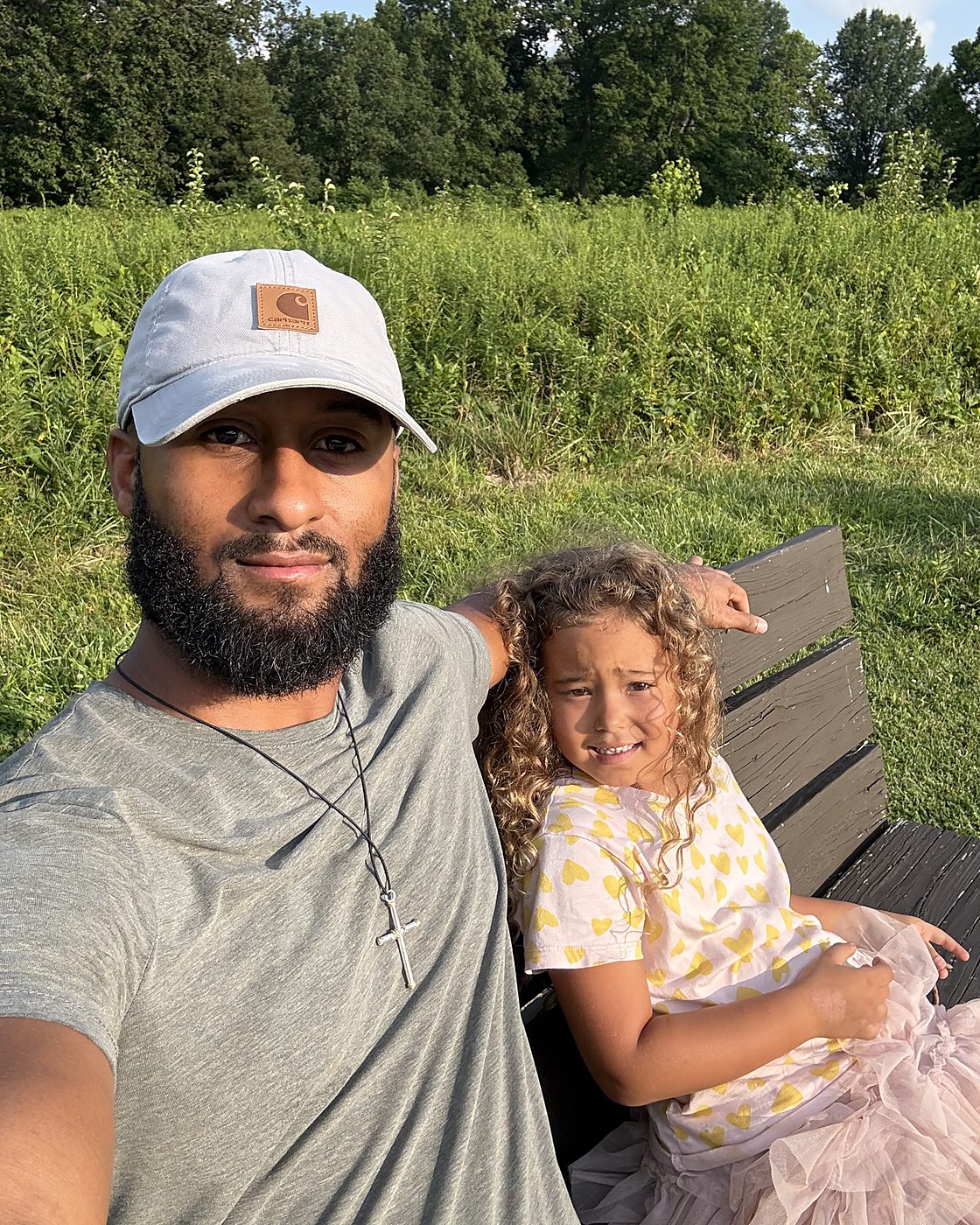 Nate and his daughter sitting together on a park bench on a summer evening